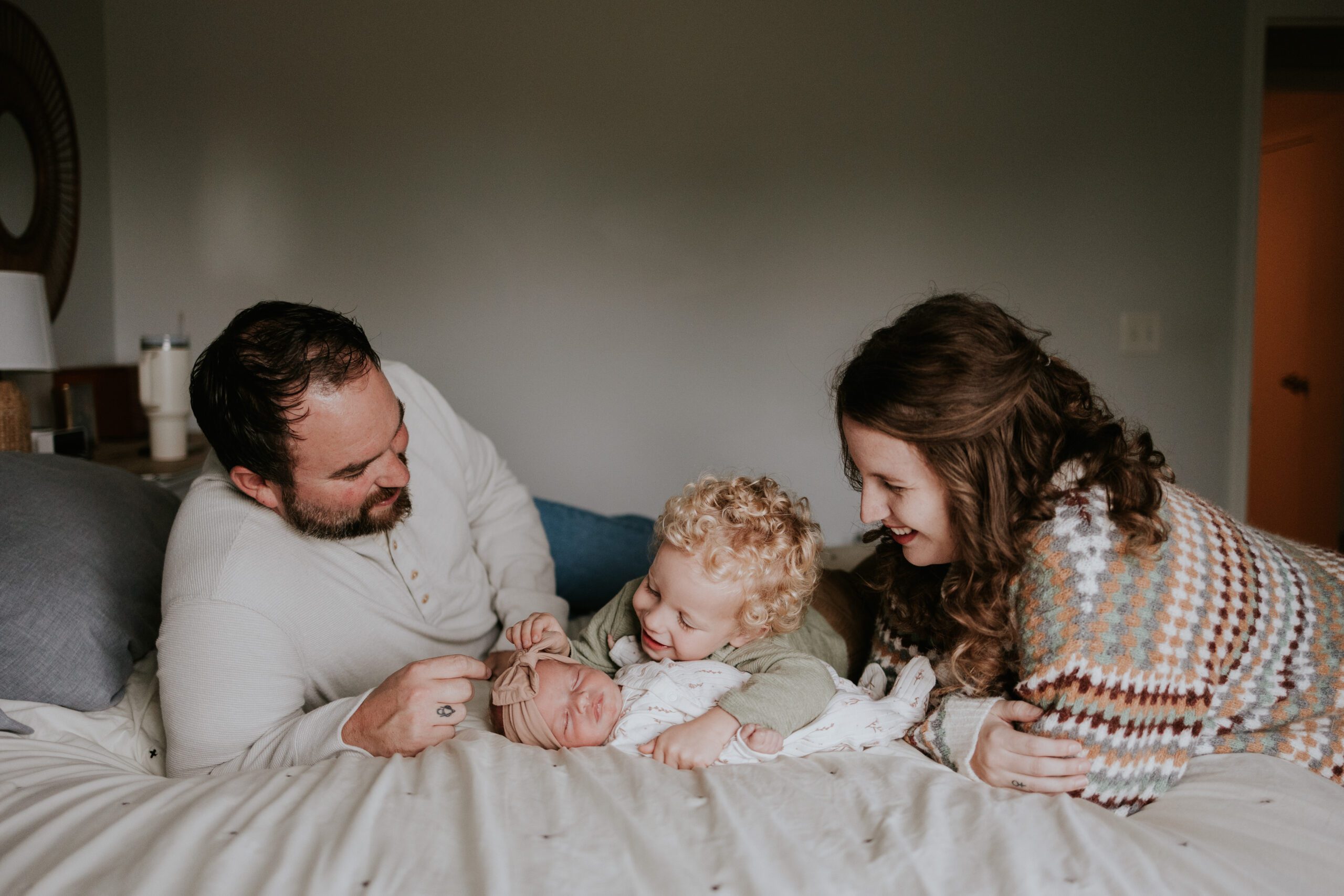 Family snuggled on a bed adoring their newborn baby.