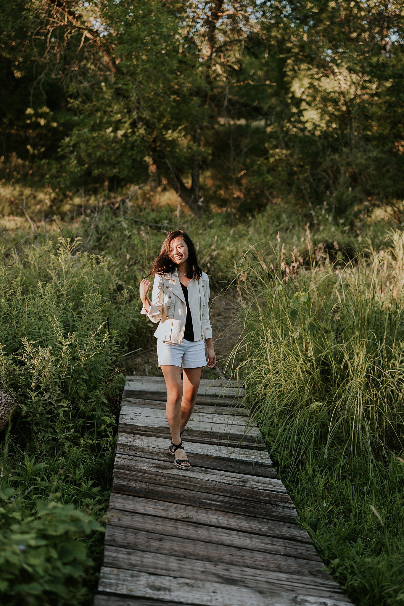Senior photography near Le Mars Iowa of a Girl walking across a bridge. She is smiling and playing with her hair while the sun comes in from the left and shines on her face. 
